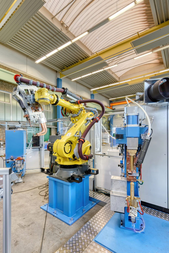 Ein Handling-Roboter führt das Bauteil zu einem DALEX-C-Modul. Dort werden die Rundschweißmuttern zugeführt und automatisch mittels Buckelschweißen auf dem Bauteil fixiert.